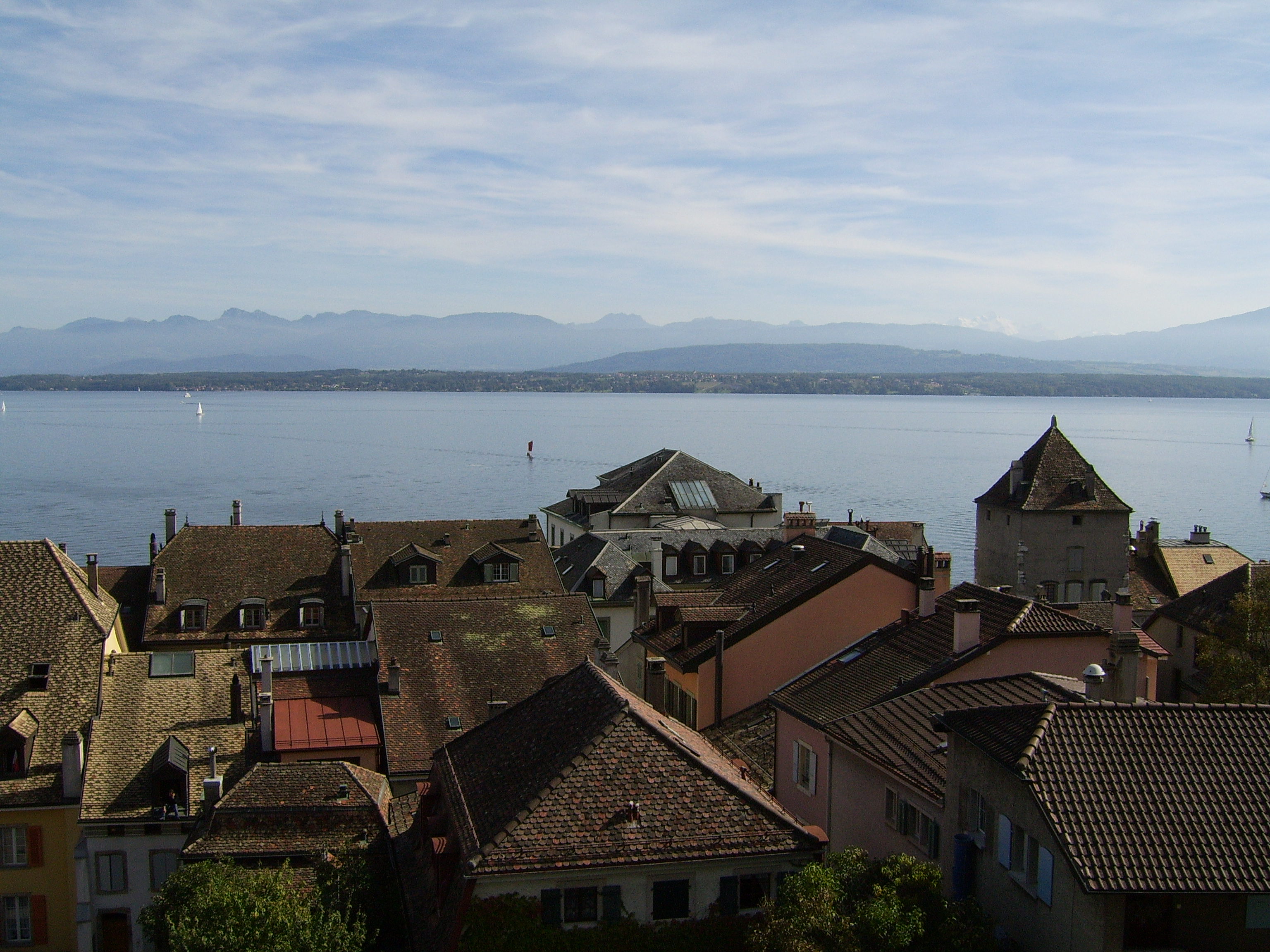 A photo of mountains in the distance, with Lake Geneva in the middle ground and rooftops of Nyon in the foreground.